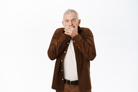 Shocked mature man, old male model looking speechless and stunned at camera, standing over white backgroundの写真素材