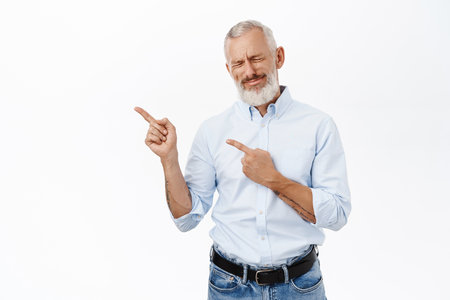Senior business man pointing fingers left, showing advertisement, promo offer, standing over white backgroundの写真素材