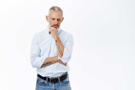 Thoughtful businessman looking down and thinking, pondering with serious face expression, making decision, standing over white backgroundの写真素材