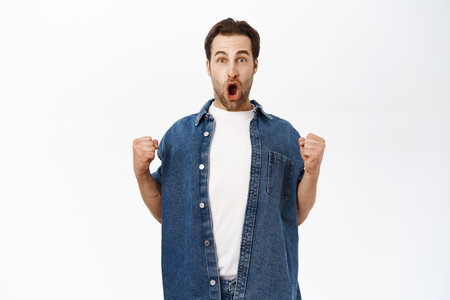 Image of enthusiastic adult man winning and celebrating victory, achieve goal, scream wow in delight, triumphing, standing over white backgroundの写真素材