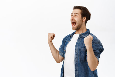 Happy guy winning, triumphing, looking at smth and celebrating victory. Sports game fan achieves goal, enjoyes victory, stands over white backgroundの写真素材