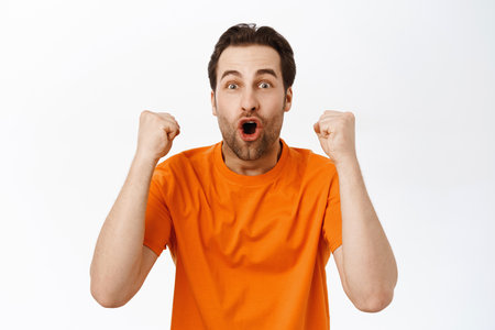 Image of enthusiastic adult man winning, celebrating victory, smiling and screaming with excitement, achieve goal, triumphing, standing over white backgroundの写真素材