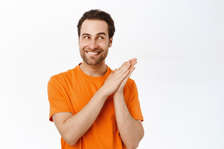 Enthusiastic smiling man rubbing hands and looking pleased, scheming smth, having plan, standing over white backgroundの写真素材