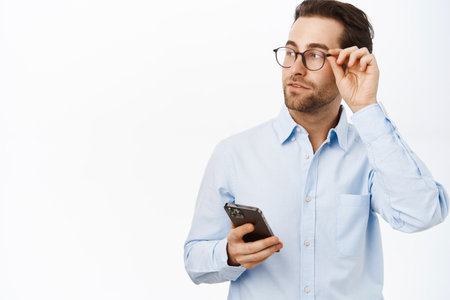 Handsome male entrepreneur using mobile phone, standing in glasses and blue shirt over white backgroundの写真素材