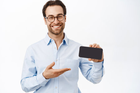 Handsome european businessman presenting new app, showing smartphone application, standing over white backgroundの写真素材