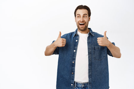 Handsome smiling bearded man, shows thumbs up, approve smth, recommending product, praise or compliment you, standing over white backgroundの写真素材