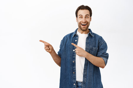 Portrait of handsome smiling adult man, pointing fingers left, showing way, promo on copy space, product banner, standing over white backgroundの写真素材