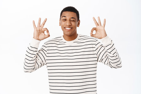 Happy smiling african american adult man, showing okay, ok sign, approve smth good, praise or compliment, standing over white backgroundの写真素材