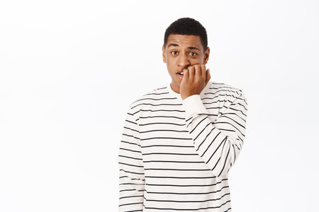 Anxious middle aged african american man, biting fingers, looking scared or nervous, standing over...