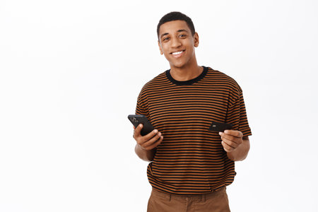 Online shopping. Happy smiling man registrating his credit card on mobile phone app, using application to buy smth, standing over white backgroundの写真素材