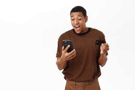 Online shopping. Happy smiling man registrating his credit card on mobile phone app, using application to buy smth, standing over white backgroundの写真素材