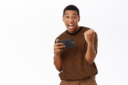 Excited smiling african american man playing on mobile phone, looking at smartphone with happy face, white backgroundの写真素材
