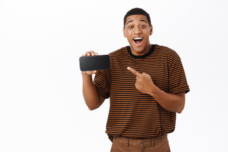 Excited Black man pointing at his mobile phone, showing smartphone screen and smiling, recommending application or website, white backgroundの写真素材