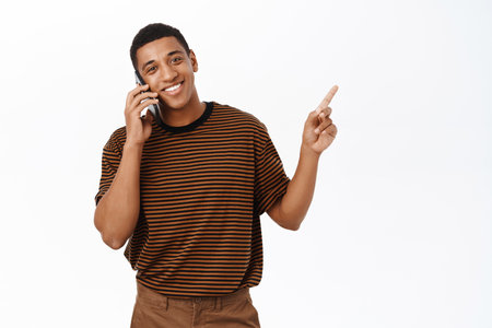 Smiling african american man talking on mobile phone and pointing at banner, showing cellular company advertisement, white backgroundの写真素材