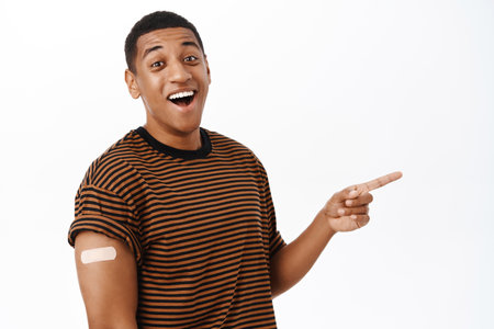 Health and vaccination concept. Vaccinated african american man pointing at banner info, showing advertisement on copy space, white backgroundの写真素材
