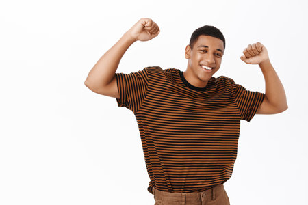 Image of handsome maculine Black man dancing, raising hands up and looking confident, feeling upbeat, standing over white backgroundの写真素材