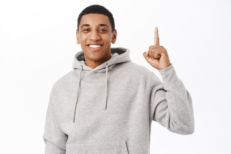Close up of smiling, happy Black man pointing fingers up, showing avertisement, banner on top, standing over white backgroundの写真素材