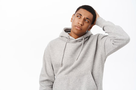 Portrait of Black man scratches his head and looks puzzled, thinks with confused face, stands over white backgroundの写真素材
