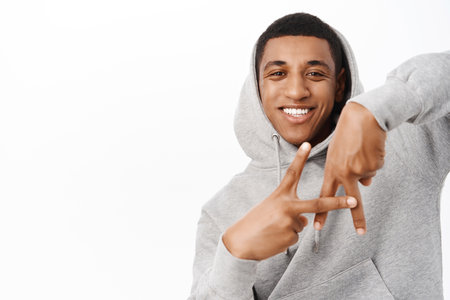 Good looking african american man shows LA finger gesture, standing in grey hoodie over white backgroundの写真素材