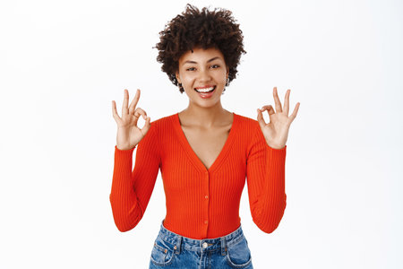 Portrait of beautiful young woman, 25 years old, shows okay, ok sign and smiles, approves smth, recommends product, stands over white backgroundの写真素材