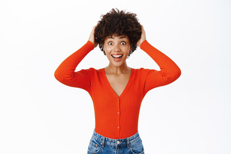 Woman with surprised face, touches her curly hair and looks amazed, stands over white backgroundの写真素材
