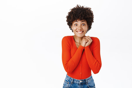 Image of african american girl looks excited, tempted to see smth, feeling enthusiastic, standing over white backgroundの写真素材