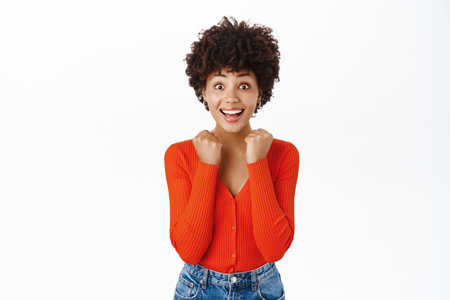 Enthusiastic african american woman jumps from excitement, looks surprised and thrilled, stands over white backgroundの写真素材
