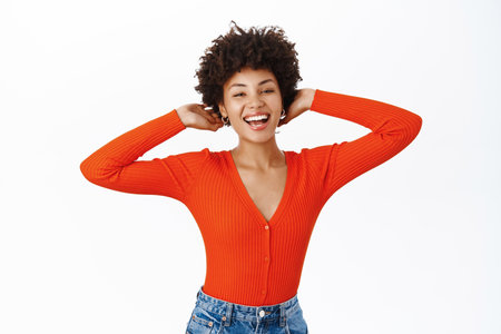 Carefree woman touches her new haircut, smiles and looks happy, stands over white backgroundの写真素材