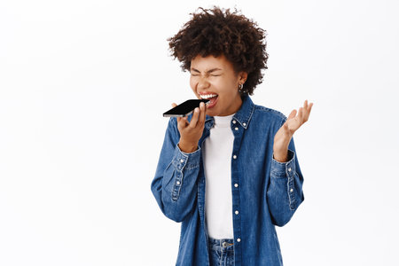 African american woman screaming in speaker of her phone, shouting at mobile phone voice message, white backgroundの写真素材