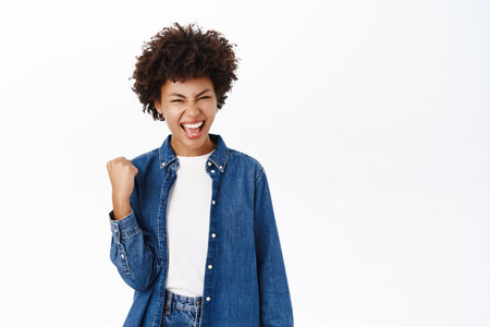 Enthusiastic african american woman winning and rejoicing, celebrating victory, success concept, achieve goal and triumphing, white backgroundの写真素材
