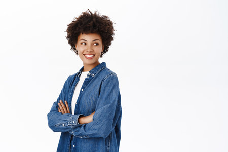 Portrait of stylish african american girl, cross arms on chest, looks happy and confident, concept of students and young professionals, white backgroundの写真素材