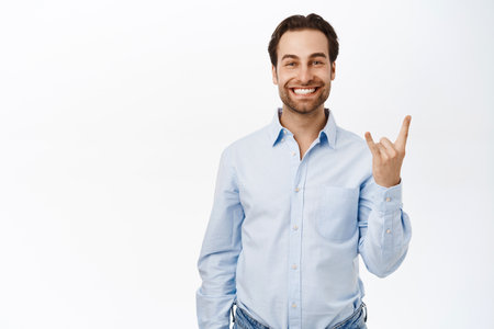 Happy office guy shows rock on, heavy metal horns sign and smiles pleased, has fun, stands over white backgroundの写真素材
