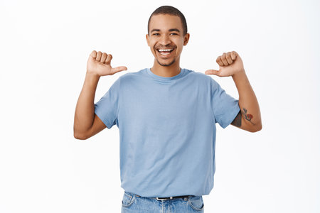 Confident arab man pointing at himself and smiling, feeling self-assured, standing in blue tshirt over white backgroundの写真素材
