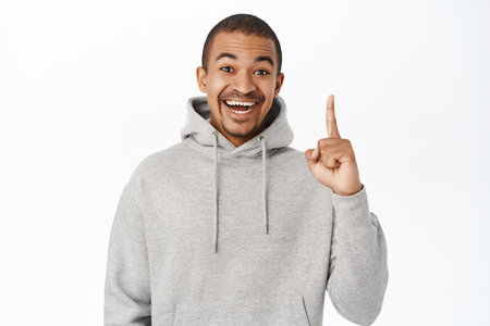 Happy smiling man pointing finger up at logo, showing advertisement or banner on top, standing against white backgroundの写真素材