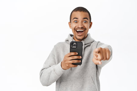 Portrait of smiling guy taking photos on smartphone, recording video on mobile phone camera, standing over white studio backgroundの写真素材