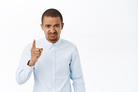 Angry bossy man shaking finger and looking with disapproval, scolding employee, stands over white backgroundの写真素材