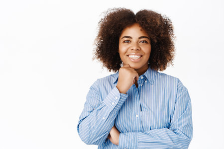 Young smiling african american woman in blue collar shirt, looking with interest and hope, listetning with joy, standing over white backgroundの写真素材