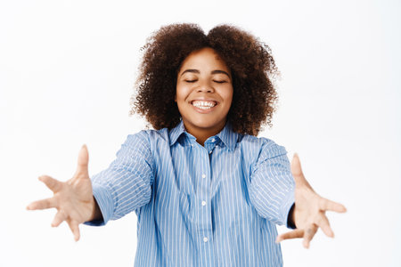 Smiling african american woman stretching out hands to reach smth, stands over white backgroundの写真素材