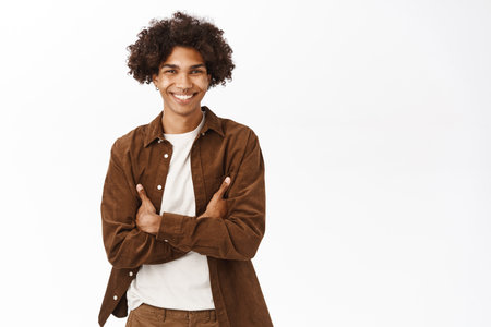 Portrait of hispanic college boy, smiling and looking happy, cross arms on chest, confident and relaxed pose, standing over white backgroundの写真素材
