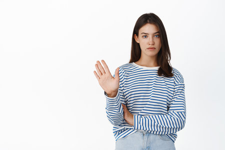 Image of serious reluctant girl rejecting, waving hand to give negative answer, refusing, being unamused of offer, standing against white backgroundの写真素材