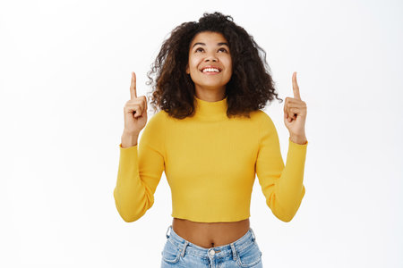 Enthusiastic young african woman, pointing finger up, showing advertisement, top promo banner, logo upwards, standing over white backgroundの写真素材
