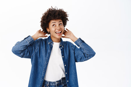 Beautiful modern african american girl, touches her curly hair, new hairstyle, smiling happy, standing over white backgroundの写真素材