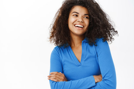 Portrait of beautiful young african american woman with shiny, curly healthy hair, posing happy, smiling, standing on white banner backgroundの写真素材