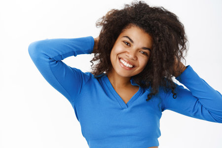 Portrait of beautiful young african american woman with shiny, curly healthy hair, posing happy, smiling, standing on white banner backgroundの写真素材