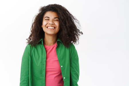 Portrait of beautiful young Black woman smiling, looking happy and carefree, daydreaming, standing in casual clothes over white backgroundの写真素材