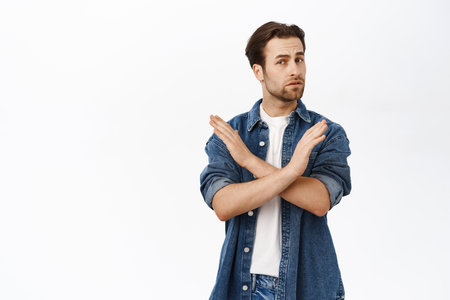 Portrait of adult man shows cross, stop sign, disapprove smth, dislike and reject, prohibit action, say no, stands over white backgroundの写真素材