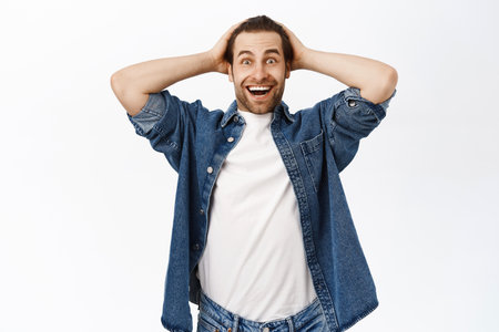 Image of guy looks happy and surprised, receive great news, smiles with disbelief, stands over white backgroundの写真素材