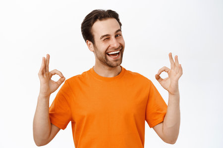Portrait of handsome happy guy shows okay sign, stands in orange tshirtの写真素材