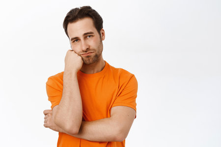 Man thinking, looking complicated, dreaming of smth, standing in orange tshirt over white backgroundの写真素材