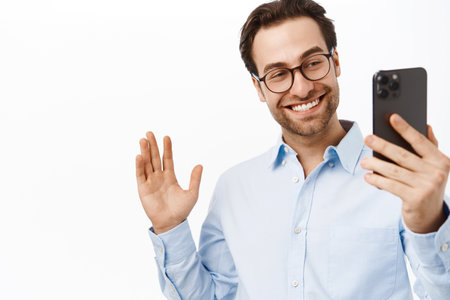 Handsome businessman demonstrating smth on video call. Office worker talking on mobile phone, waving hand, saying hello, white backgroundの写真素材